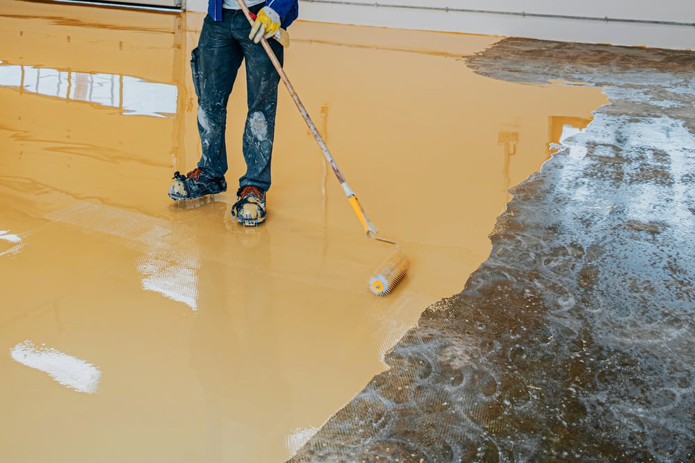 Worker, coating floor with self-leveling epoxy resin in industrial workshop.